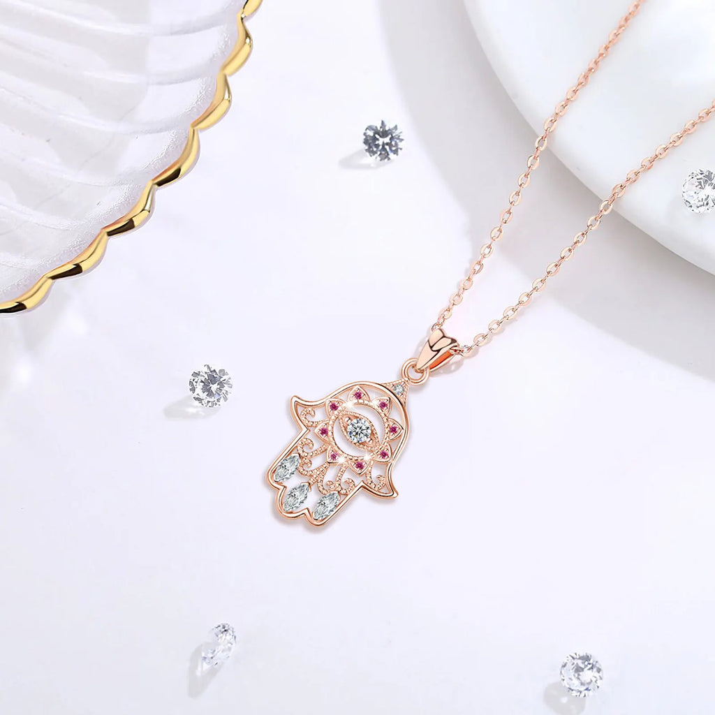 Angled rose gold-colored hamsa necklace on a white surface, showing the evil eye center and openwork hand