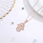 Angled rose gold-colored hamsa necklace on a white surface, showing the evil eye center and openwork hand