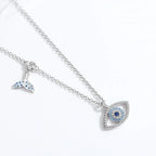 Angled flat lay of the whale tail charm and stone-set evil eye pendant on its fine chain