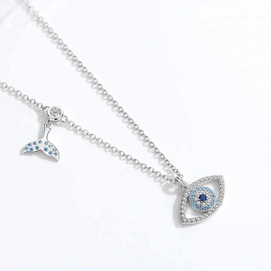 Angled flat lay of the whale tail charm and stone-set evil eye pendant on its fine chain