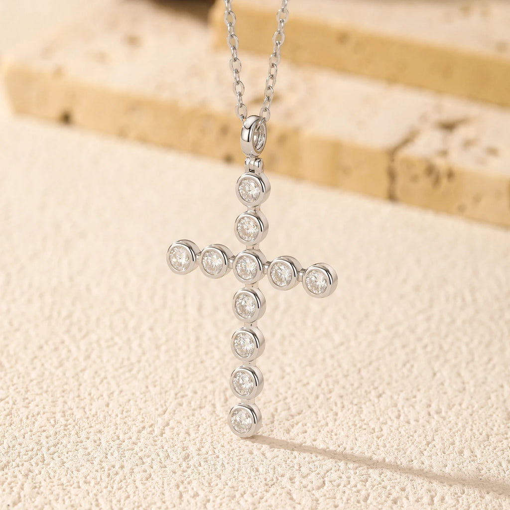 Sterling silver cross pendant with round bezel-set moissanite stones hanging against a textured backdrop