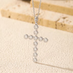 Sterling silver cross pendant with round bezel-set moissanite stones hanging against a textured backdrop