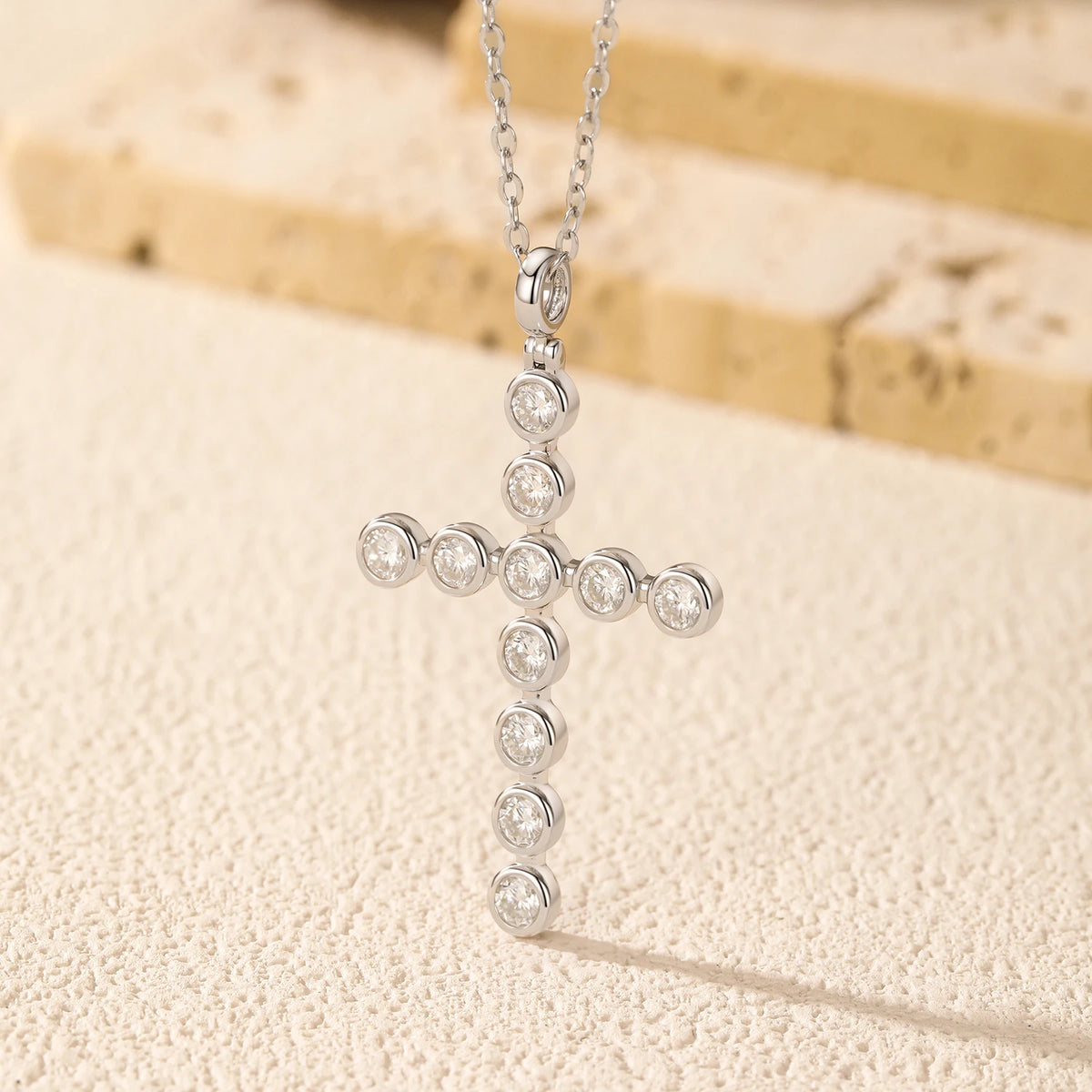 Sterling silver cross pendant with round bezel-set moissanite stones hanging against a textured backdrop