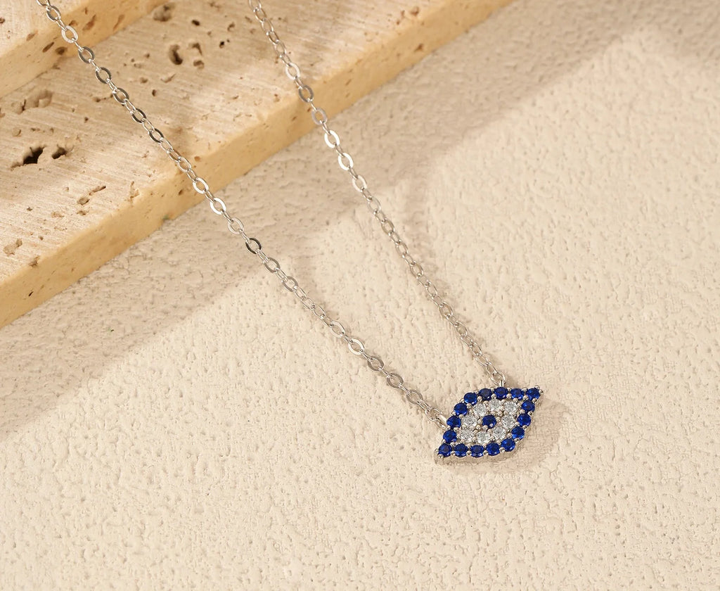 Blue and clear CZ evil eye pendant on a silver chain against a textured light surface