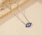 Blue and clear CZ evil eye pendant on a silver chain against a textured light surface