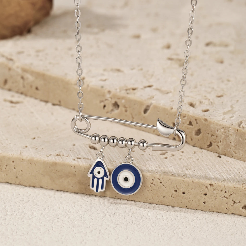 Close-up of a sterling silver pin pendant with beaded bar, blue Hamsa hand, and round evil eye