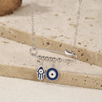 Close-up of a sterling silver pin pendant with beaded bar, blue Hamsa hand, and round evil eye