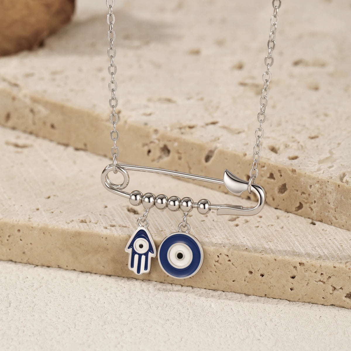 Close-up of a sterling silver pin pendant with beaded bar, blue Hamsa hand, and round evil eye
