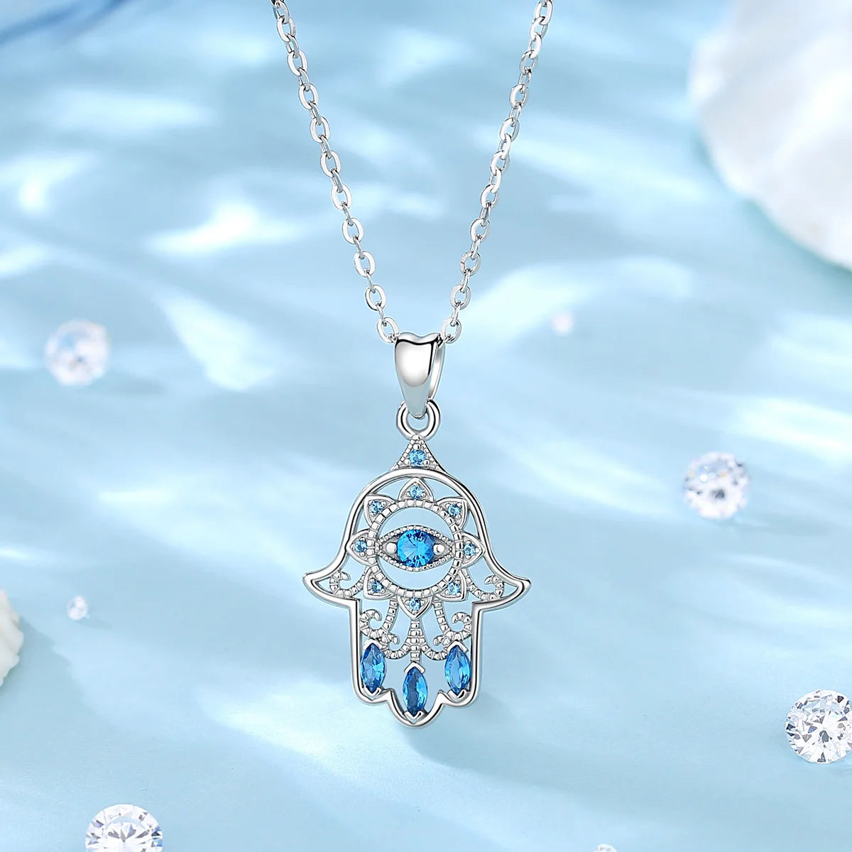 925 sterling silver hamsa necklace hanging over a blue backdrop, with blue CZ eye and lower stones