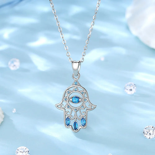 925 sterling silver hamsa necklace hanging over a blue backdrop, with blue CZ eye and lower stones