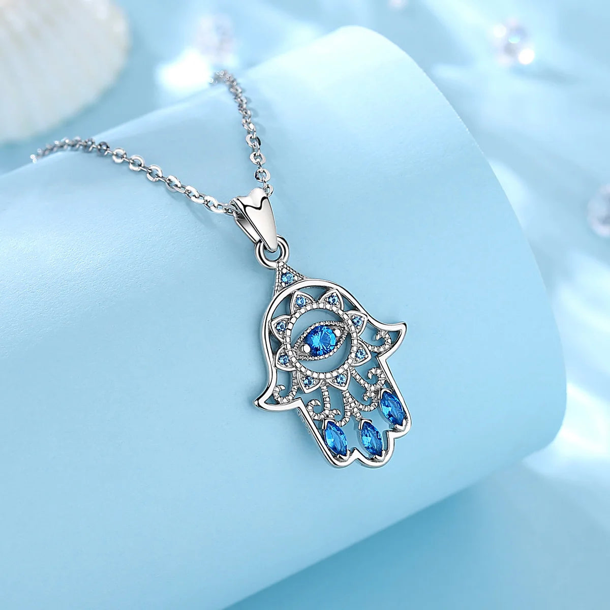 Angled close-up of the sterling silver hamsa pendant with openwork scrolls and three blue marquise CZ stones