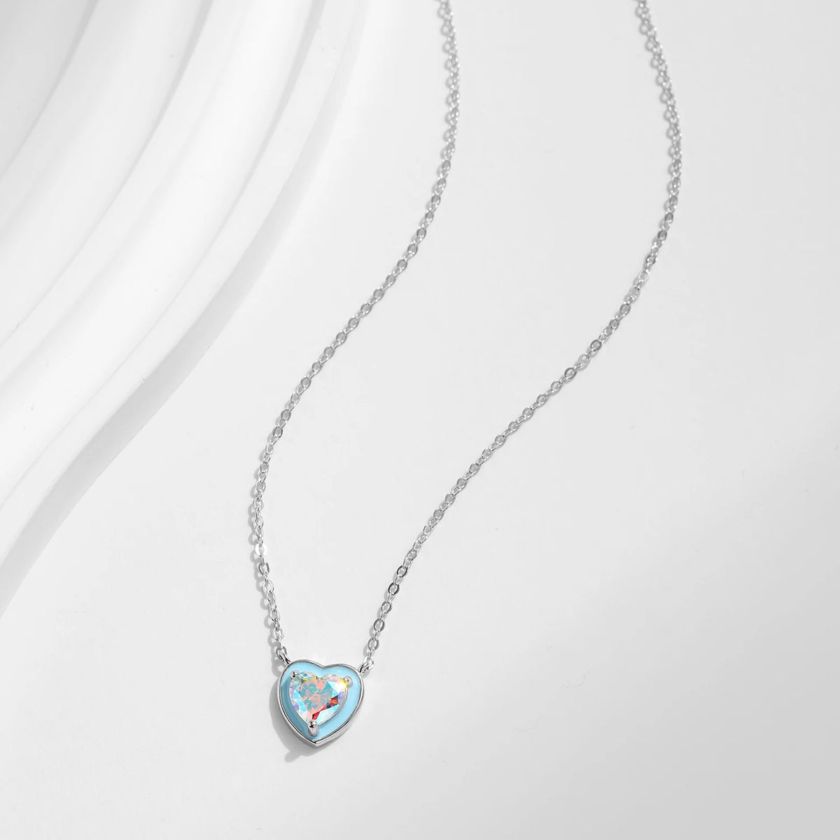 Fine oval-link chain necklace with a light blue heart and multicolored stone laid on a white surface