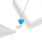 Blue opal-look heart pendant with a silver beaded border displayed against white geometric props