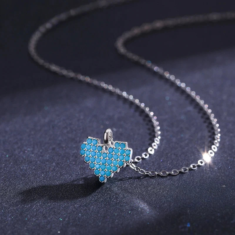 Angled close-up of the blue stone-set heart pendant and oval-link chain on dark fabric