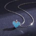 Angled close-up of the blue stone-set heart pendant and oval-link chain on dark fabric