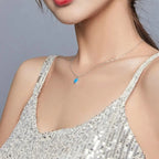 Small blue heart pendant necklace worn with a silver sequin camisole and fine oval-link chain