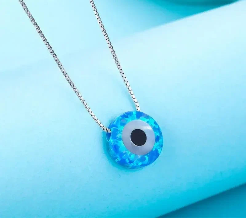 Close-up of the blue mottled synthetic opal evil eye pendant on a box chain against a blue background