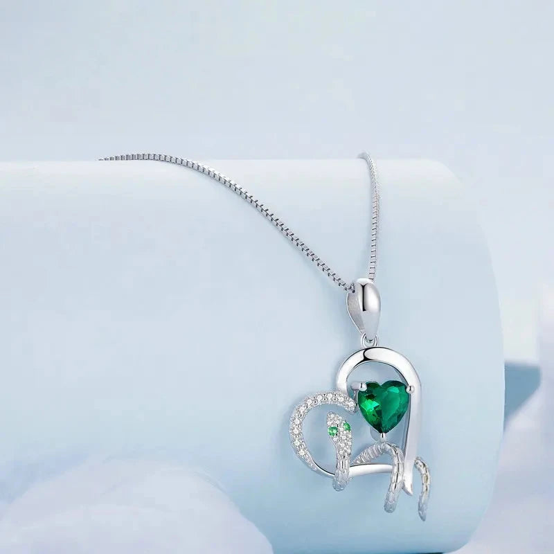 Silver snake and green heart pendant on a box chain, displayed over a pale blue cylinder