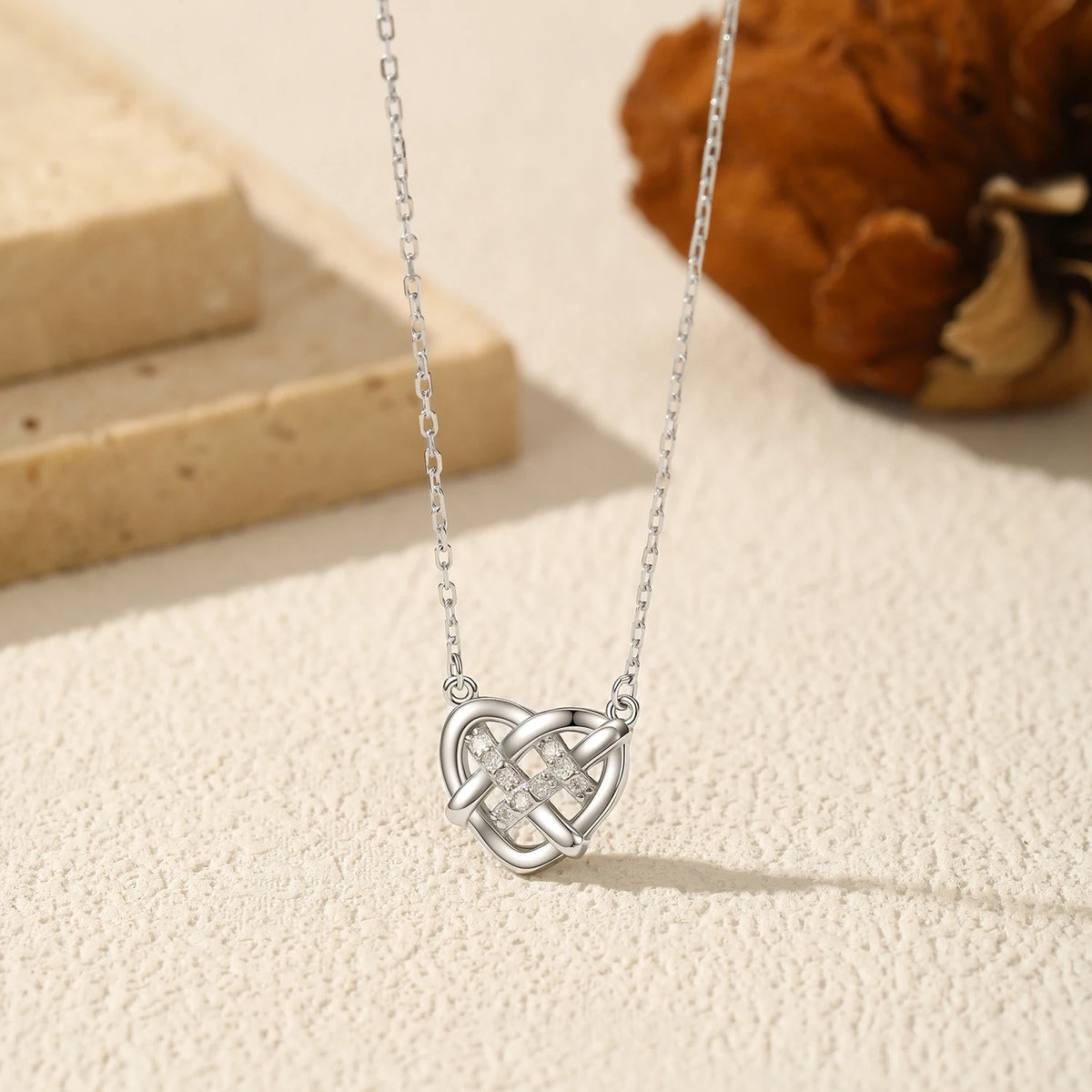 Sterling silver Celtic knot heart necklace displayed on a textured cream surface with stone props
