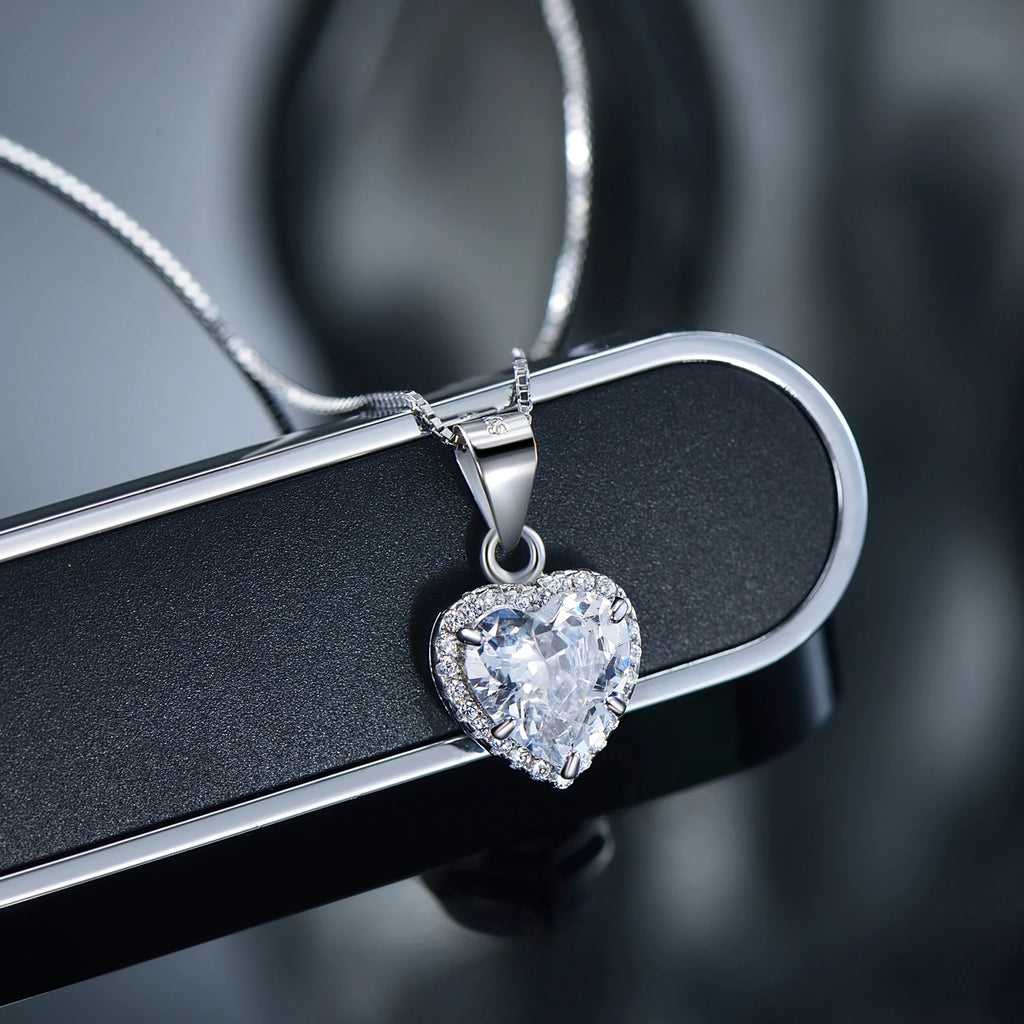 Close-up of a clear cubic zirconia heart pendant with a sparkling halo on a dark surface