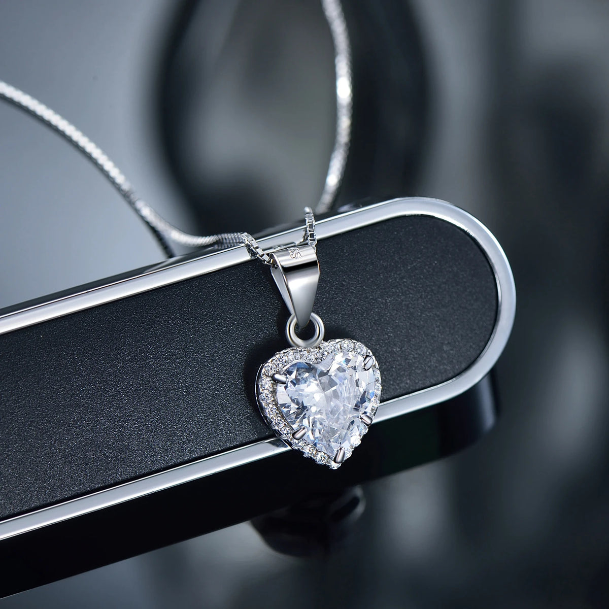 Close-up of a clear cubic zirconia heart pendant with a sparkling halo on a dark surface