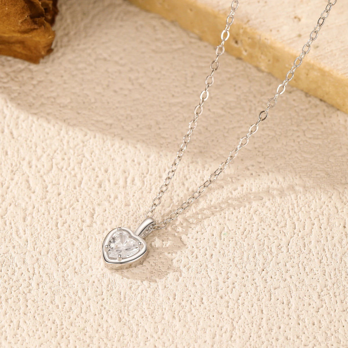 Clear cubic zirconia heart pendant in a polished sterling silver frame on a textured surface