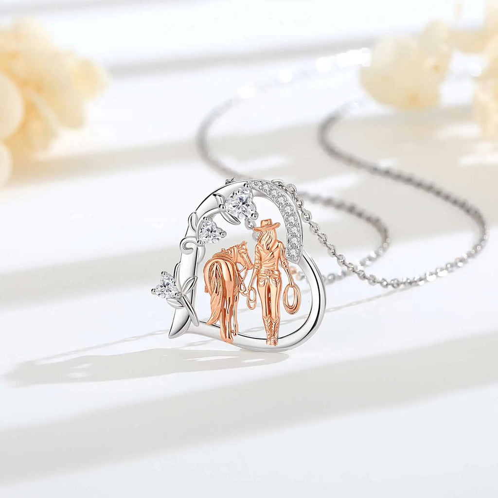 Heart-shaped cowgirl and horse pendant with clear CZ stones displayed on a white surface with the chain behind