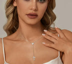 Silver cross lariat necklace worn on the neck, with a sparkling heart connector above the drop