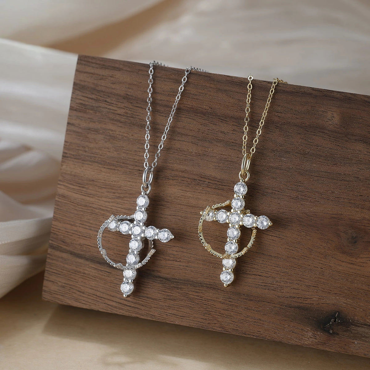 Crown of thorns cross necklaces in silver-tone and gold-tone, displayed on a wooden block
