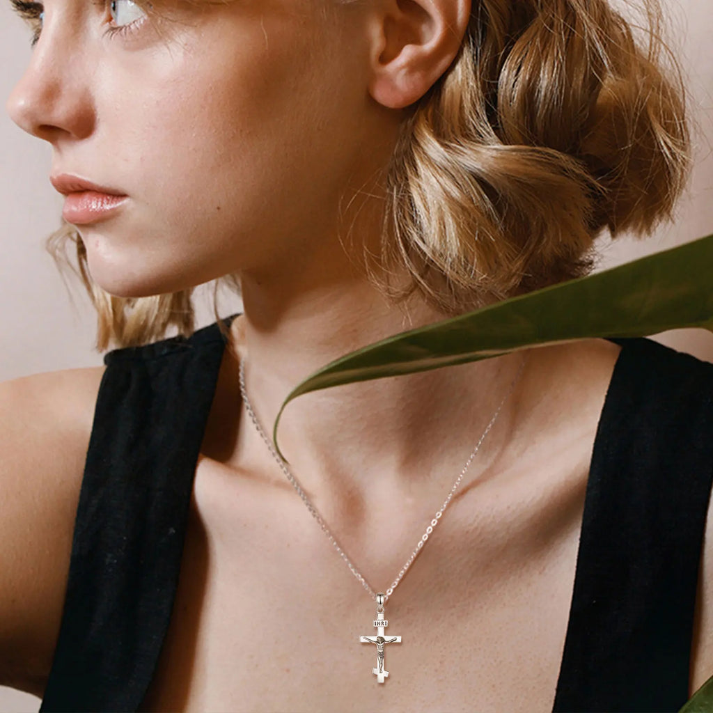 Polished sterling silver crucifix worn with a chain over a black neckline beside a green leaf