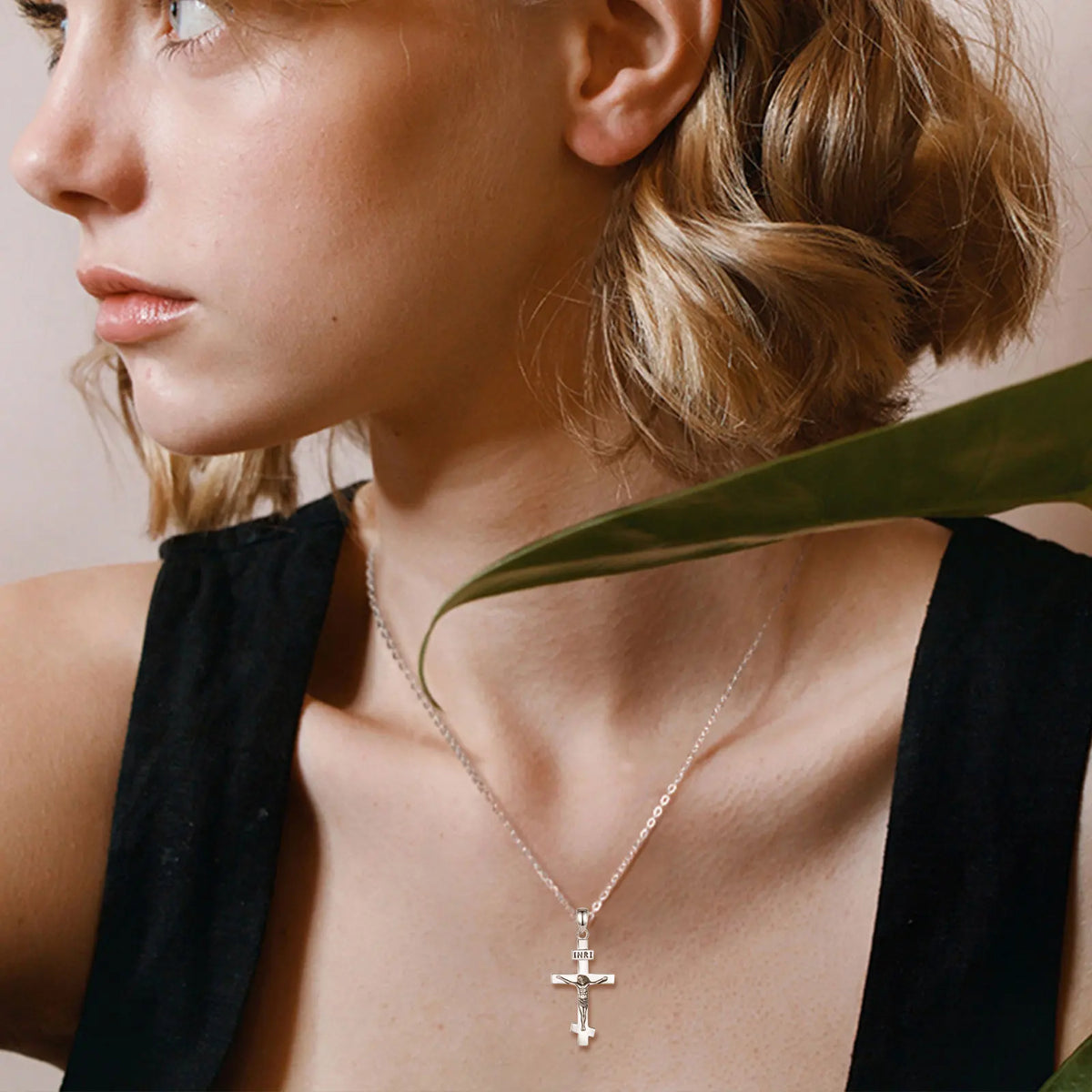 Polished sterling silver crucifix worn with a chain over a black neckline beside a green leaf