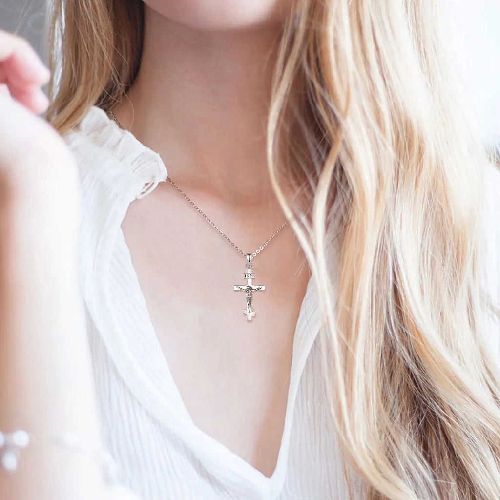 Silver crucifix necklace worn at the collarbone, showing the raised Jesus figure and INRI plaque