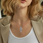 Silver crucifix pendant worn on a fine chain at the neckline, showing the detailed stepped cross