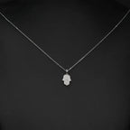 Fine oval-link necklace with a small clear CZ Hamsa pendant displayed against a black background