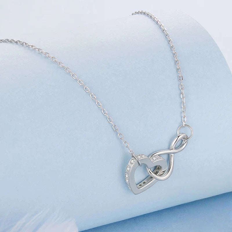 Interlocking open heart and infinity pendant with clear CZ stones on a pale blue surface