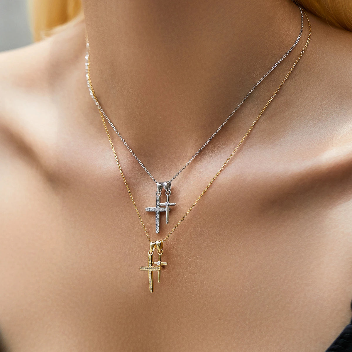 Silver-tone and gold-tone double cross necklaces worn layered at the base of the neck