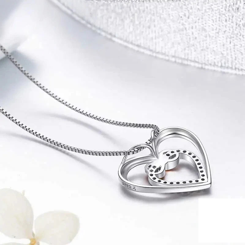 Back view of the sterling silver double-heart pendant and box chain on a white surface