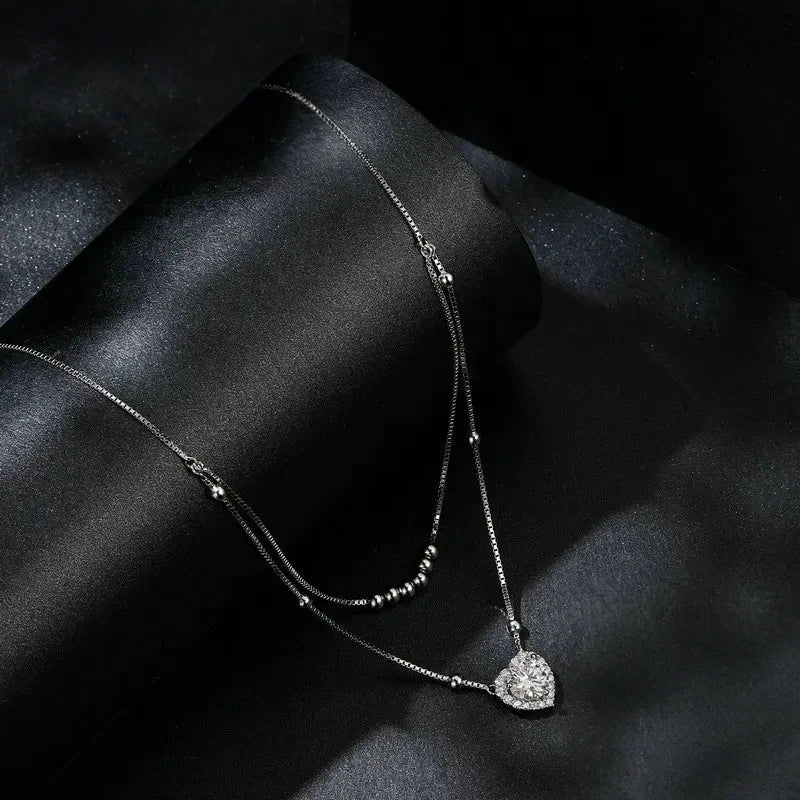 Sterling silver double-strand heart necklace displayed on black satin with a moissanite center stone
