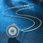 Silver-tone evil eye necklace arranged on textured blue fabric with a round colorful stone-set pendant