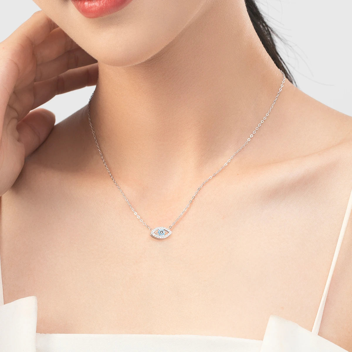 Silver-tone evil eye necklace worn at the collarbone with a blue and black stone center