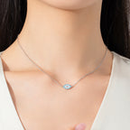 Silver-colored evil eye necklace worn at the base of the neck with blue and clear stone details