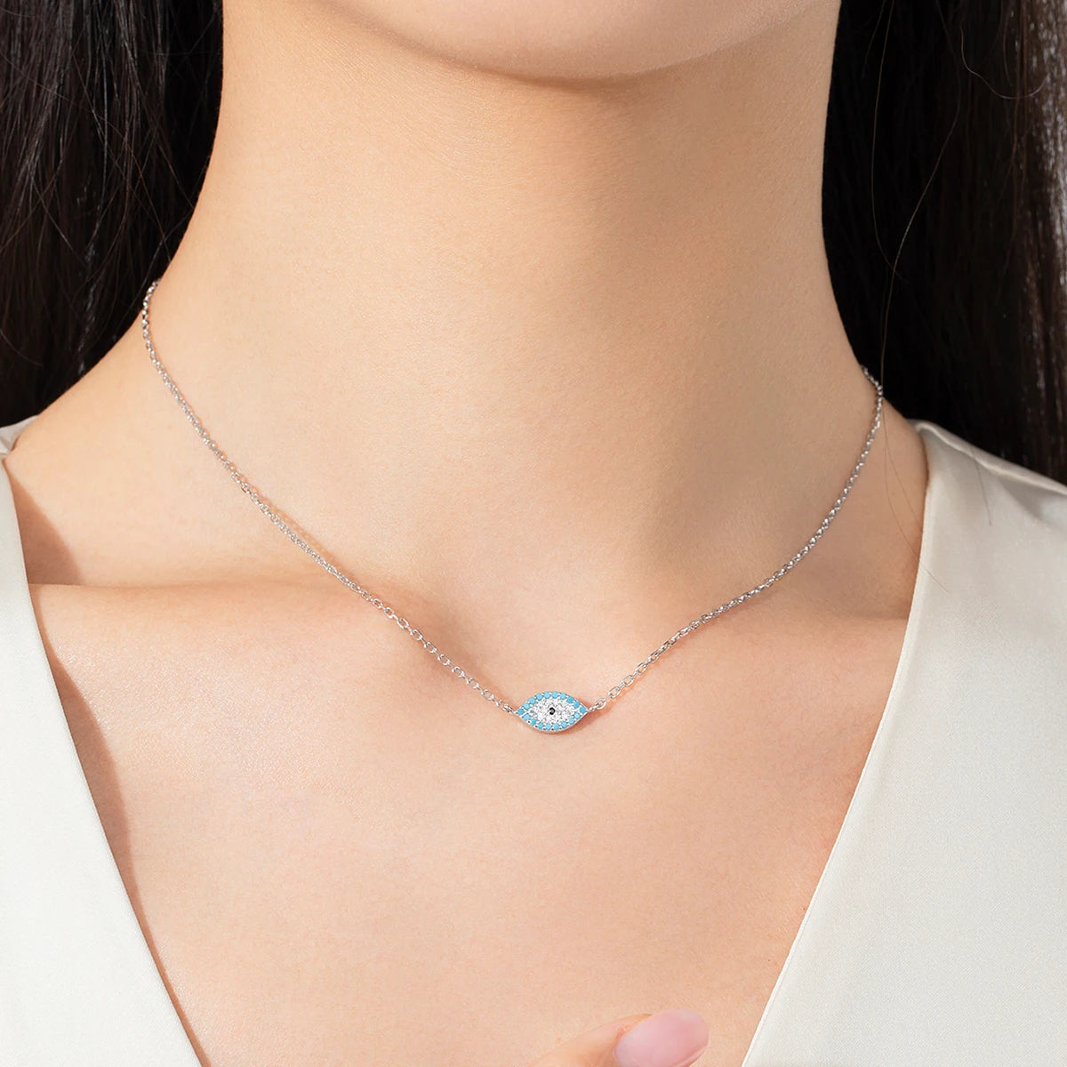 Silver-colored evil eye necklace worn at the base of the neck with blue and clear stone details
