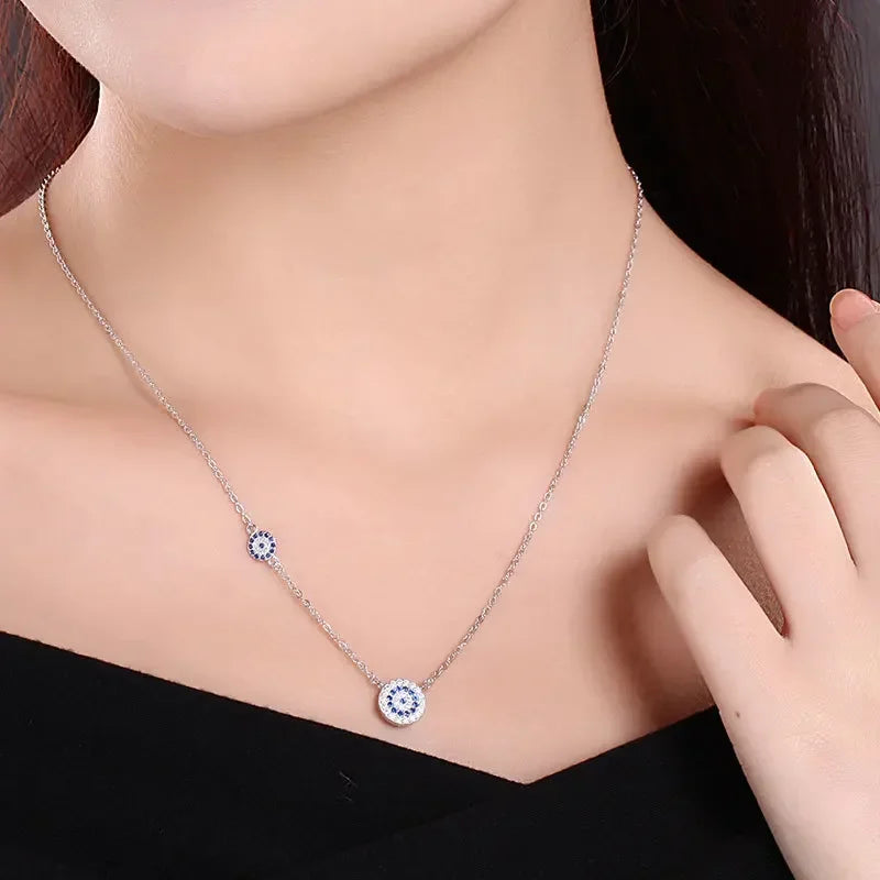 Silver-tone asymmetric evil eye necklace worn at the neckline with offset blue stone-set eye discs