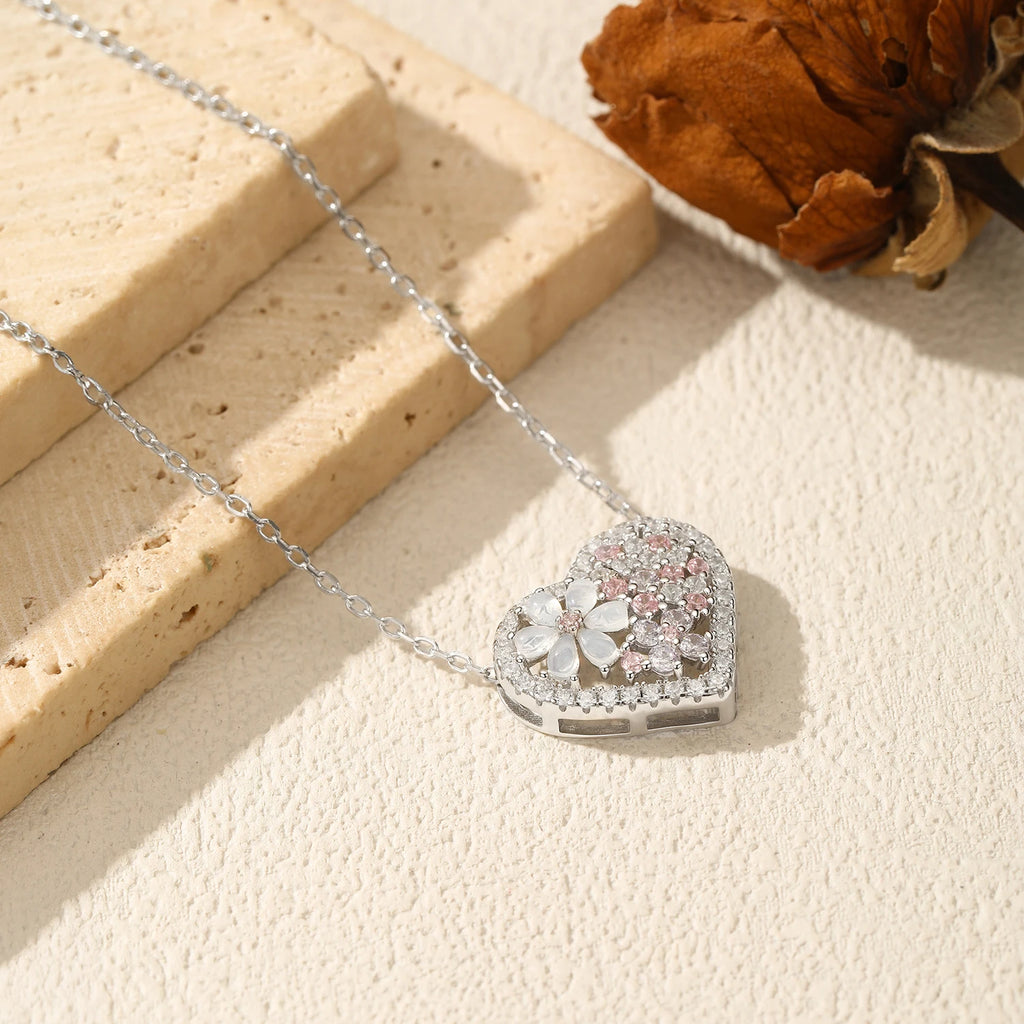 Side view of the flower heart necklace on a textured surface, showing the raised stone-set pendant
