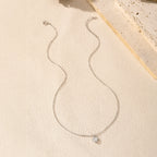 Full sterling silver heart necklace arranged on a light textured surface with the pendant centered