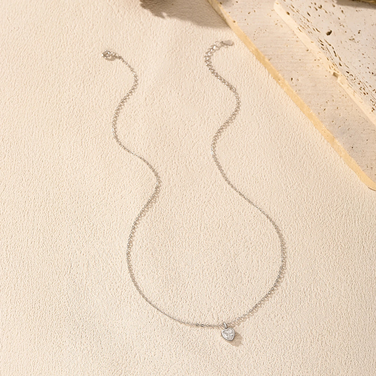 Full sterling silver heart necklace arranged on a light textured surface with the pendant centered