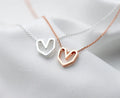 Geometric heart necklace in silver-tone and rose gold-tone finishes resting on white fabric