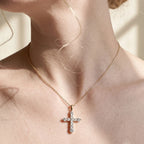 Gold-tone cross necklace with clear round stones worn at the base of the throat