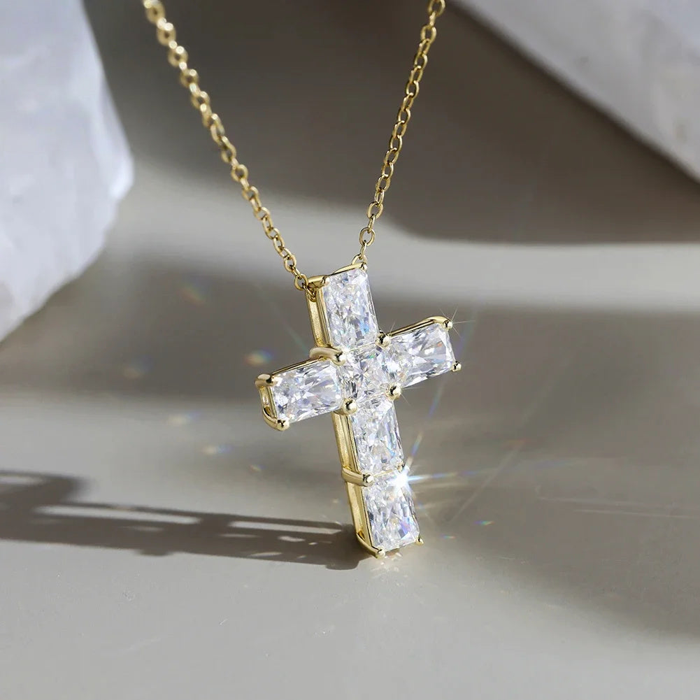 Gold-tone moissanite cross necklace suspended above a gray surface, with visible corner prongs