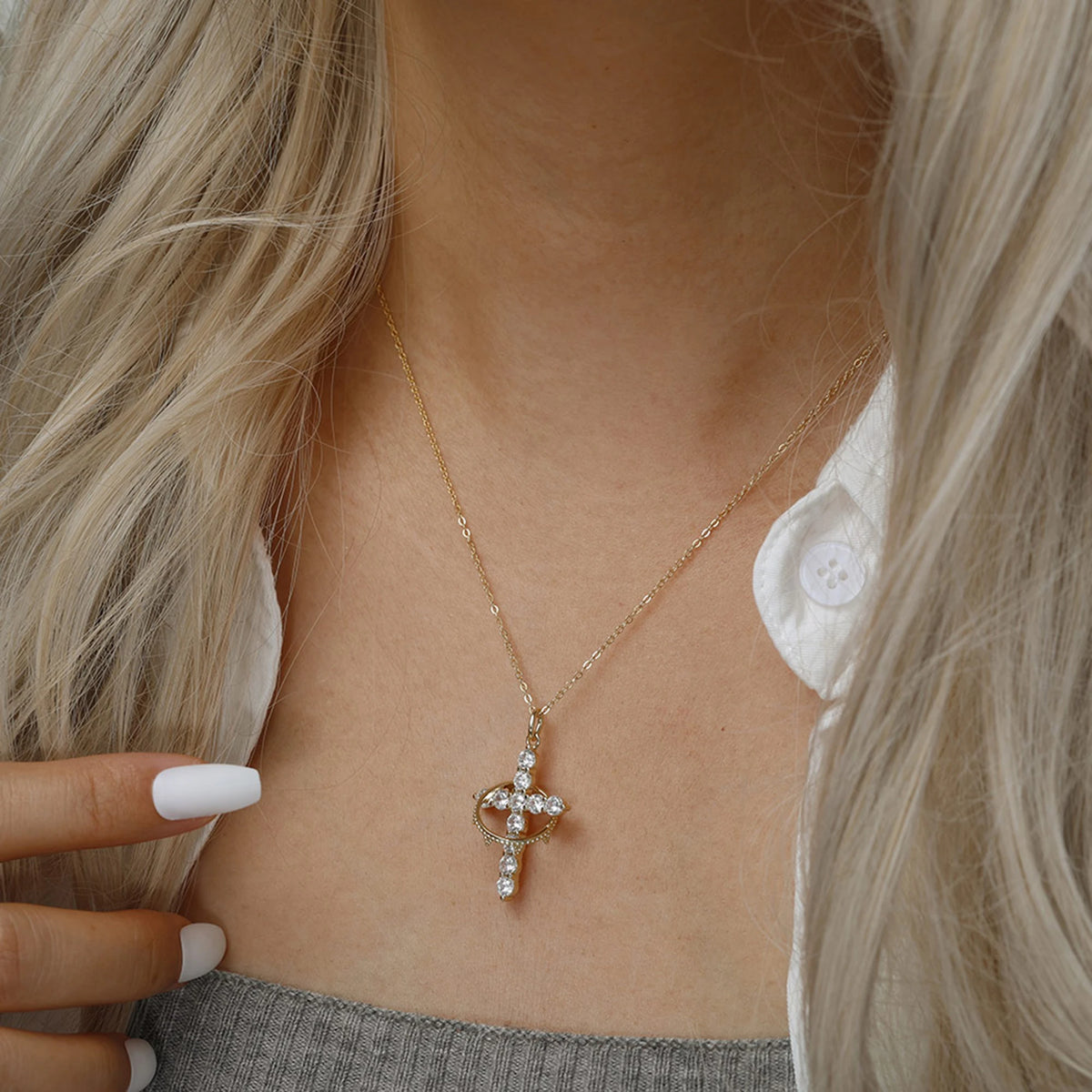 Gold-tone crown of thorns cross necklace worn with a hand pointing toward the pendant